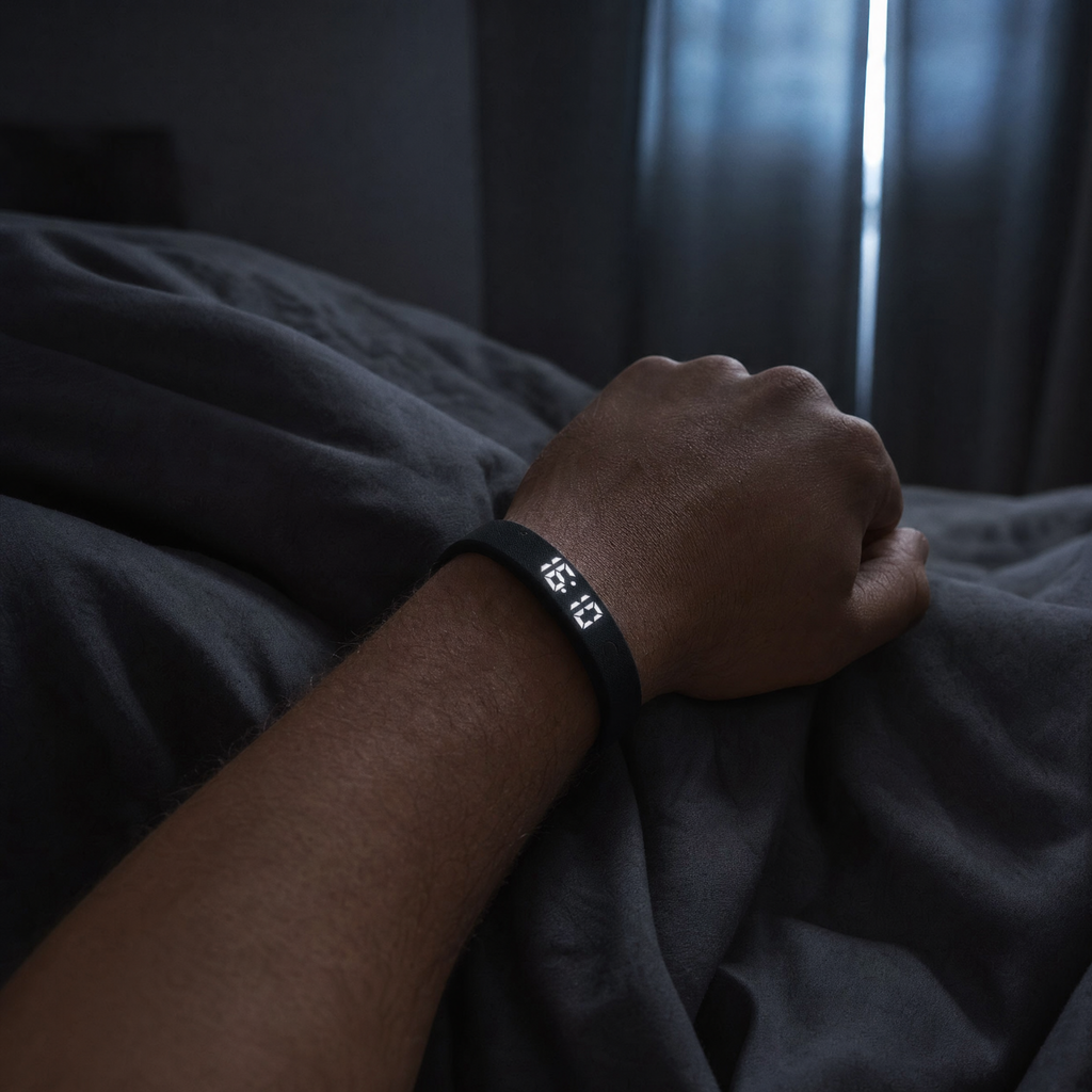 NOVIQ Wake worn on a wrist resting on a duvet in a dark bedroom before dawn, the LED display faintly lit