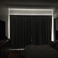 A bedroom in daytime made almost completely dark by NOVIQ Dark blackout curtains, with daylight showing only as a rim around the edges